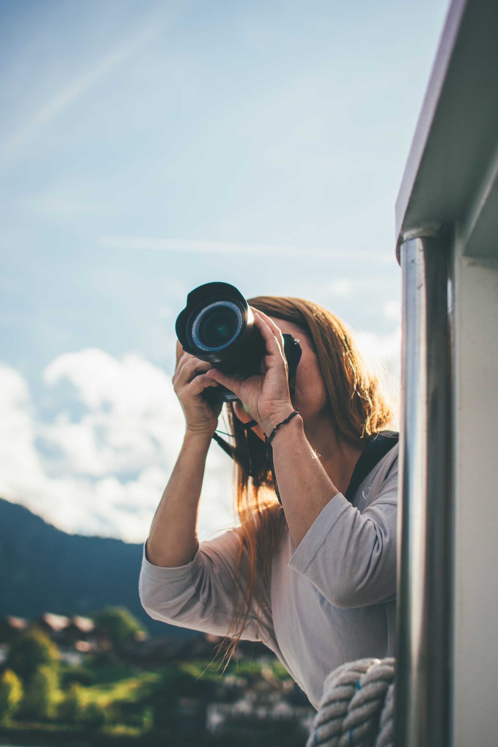 A woman uses a camera to photograph a scenic view from a boat.