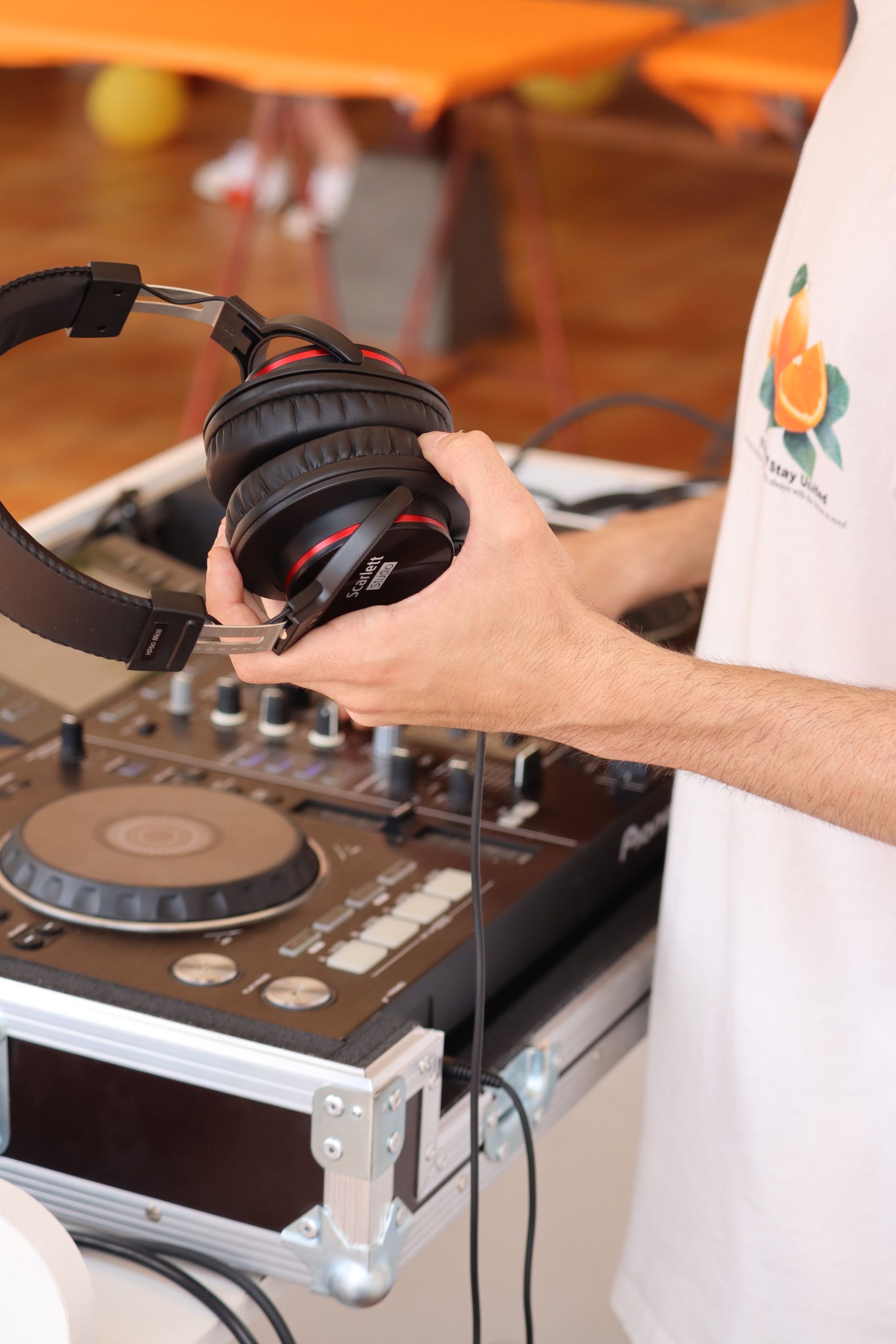 Close-up of a DJ holding headphones next to a mixer, highlighting music setup essentials.