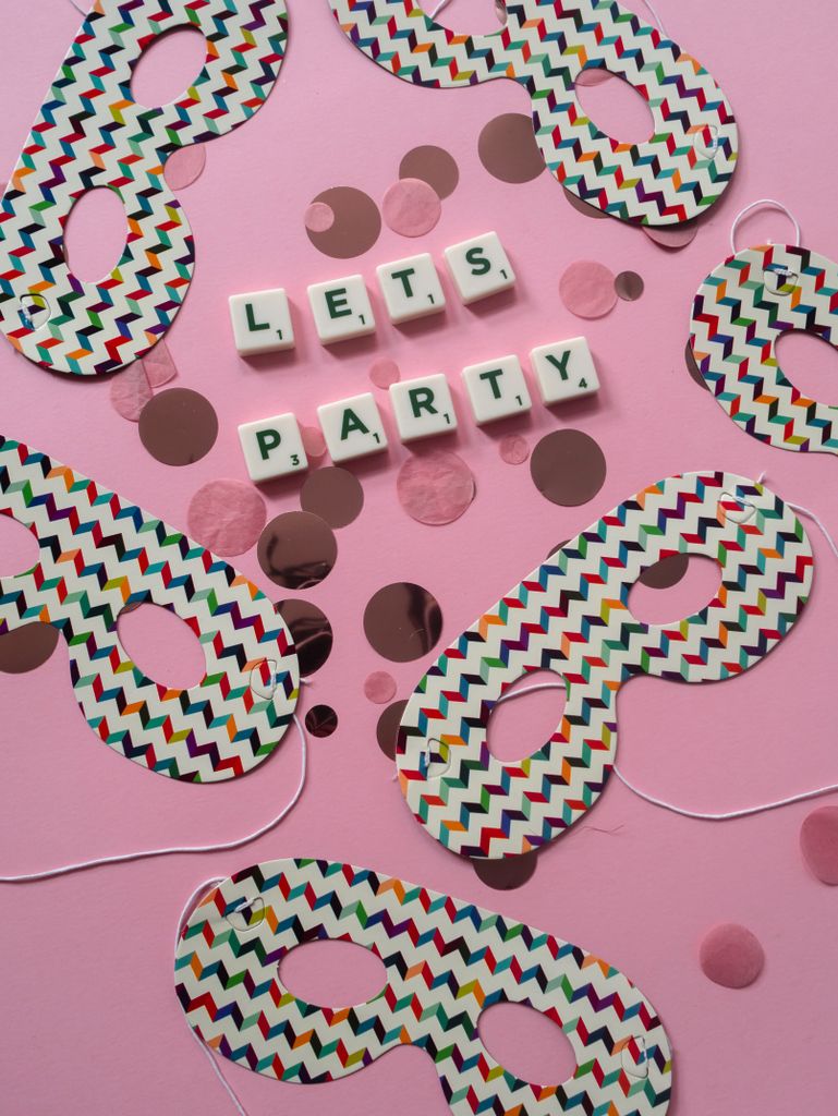 Playful flat lay with colorful masks and 'lets party' text on a pink background.