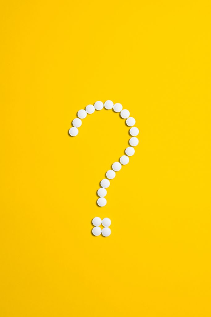 White pills arranged in a question mark shape on a bright yellow background, symbolizing medical queries.